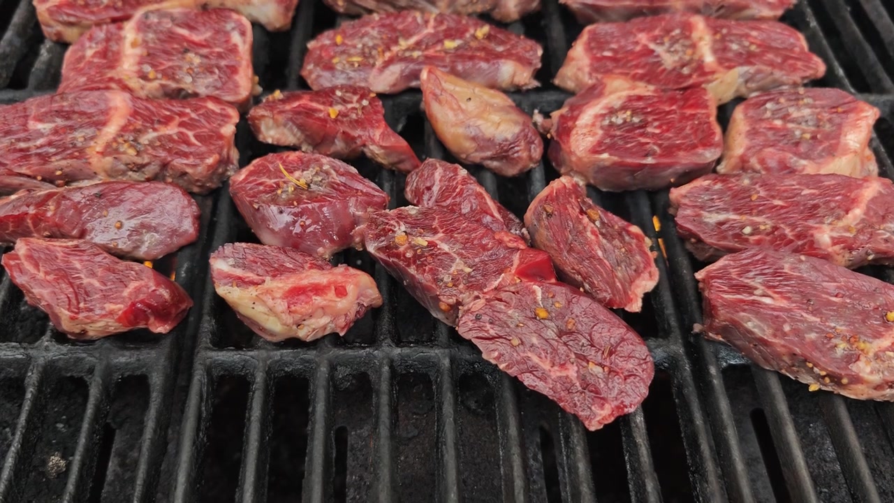 Filmato ravvicinato al rallentatore di una bistecca ben condita che cuoce su una griglia rovente, carne sfrigolante con fumo e fiamme durante una grigliata all'aperto