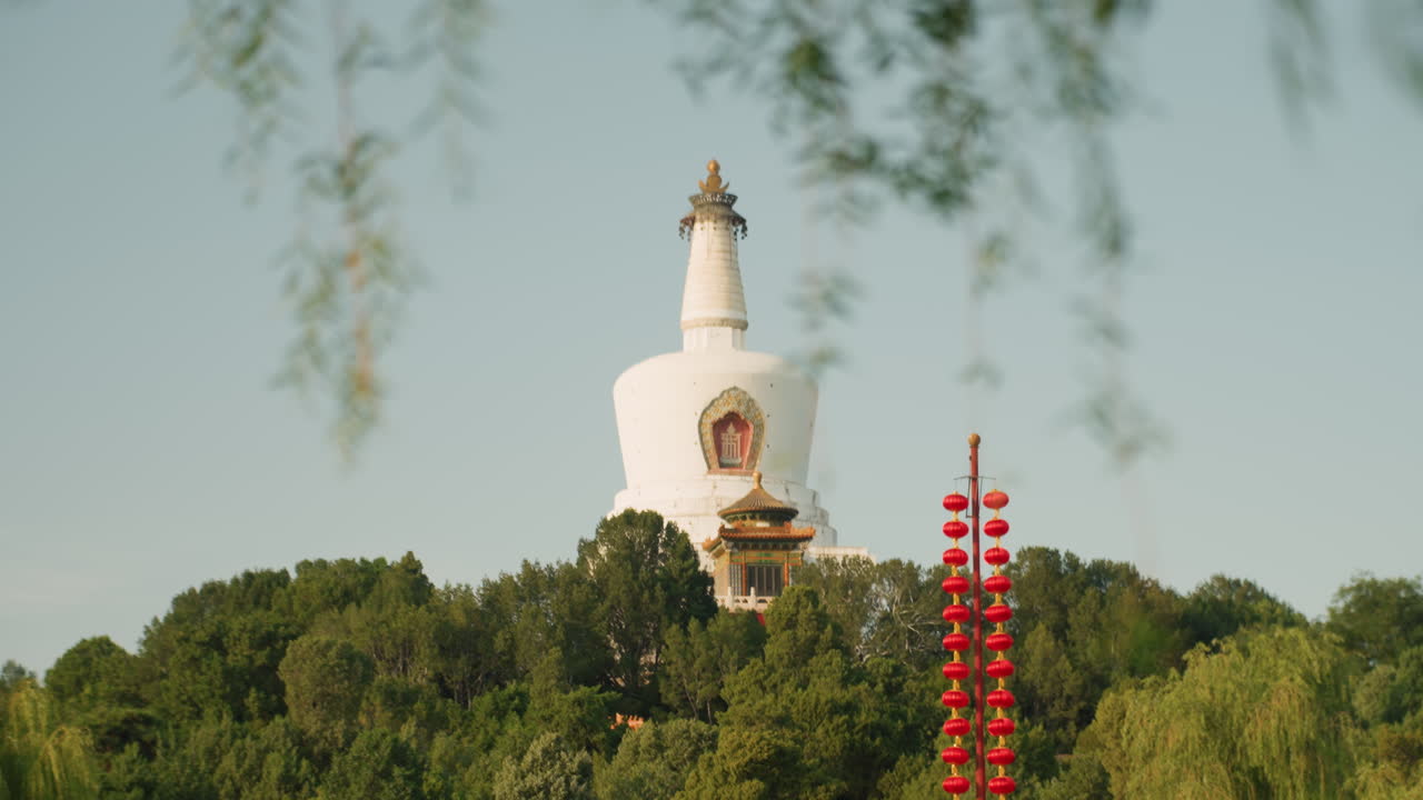 Estupa blanca enmarcada por ramas de sauce que se elevan sobre densos árboles verdes con una torre ceremonial roja en primer plano, cielo azul claro y luz solar suave crean un ambiente de viaje tranquilo y consciente, realzando la cultura budista.