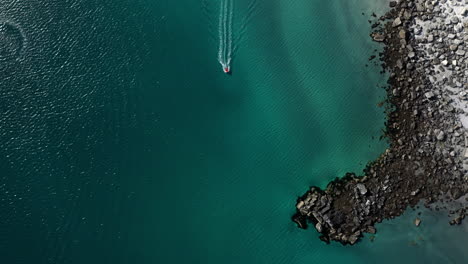 Downward-angle-drone-footage-of-a-boat-in-clear-blue-waters-at-the-island-of-Vaeroy,-Lofoten-Islands-in-Norway