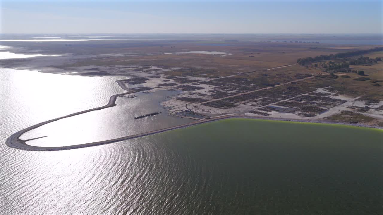 Drone wide-angle perspective from over Lago Epecuén captures the sunlit ripples of green-hued hypersaline water bordered by the abandoned spa town’s geometric grid and open salt flats, Buenos Aires