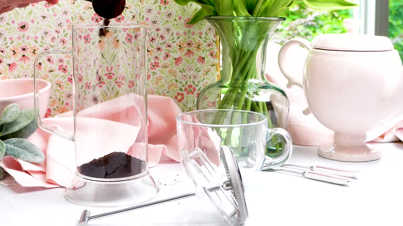 French Press made of clear glass being used to make a hot coffee. Pastel colors in a scene making hot coffee. Fresh ground coffee for brewing using a French Press method of extraction.