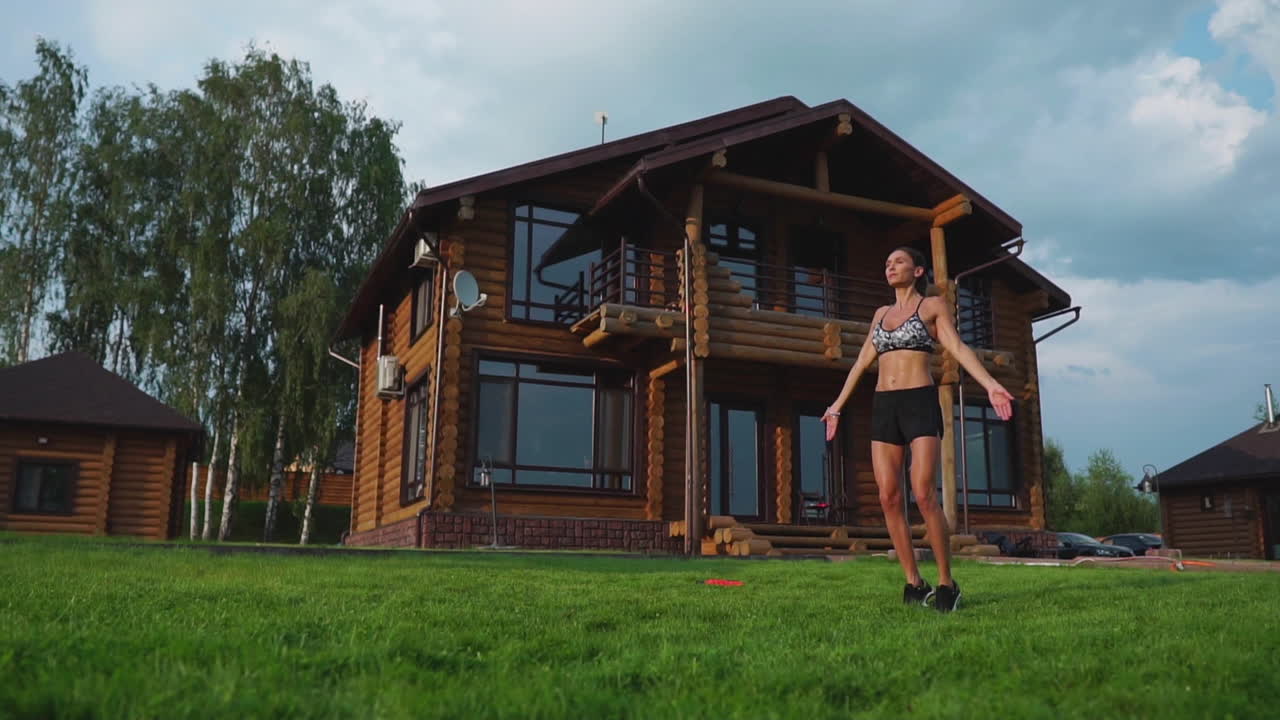 mujer delgada y hermosa en ropa deportiva en el fondo de la casa en el césped realiza saltos para el entrenamiento cardiovascular y la quema de grasa