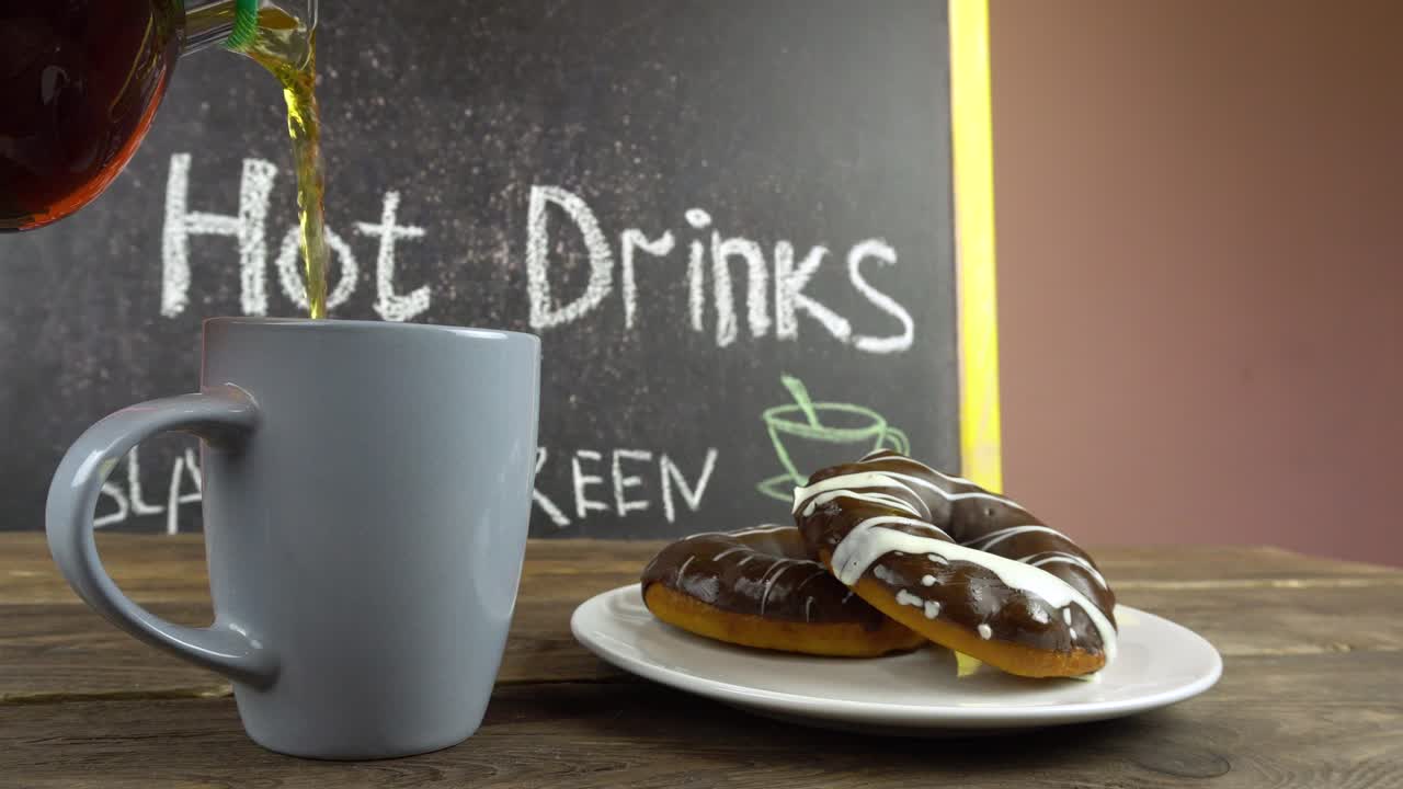 A cup of tea and donuts in chocolate glaze on a cafe table.Tea is pouring from a transparent teapot.
