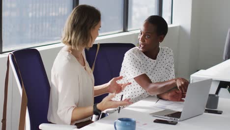 Two-diverse-female-colleagues-looking-at-laptop-and-discussing-in-office