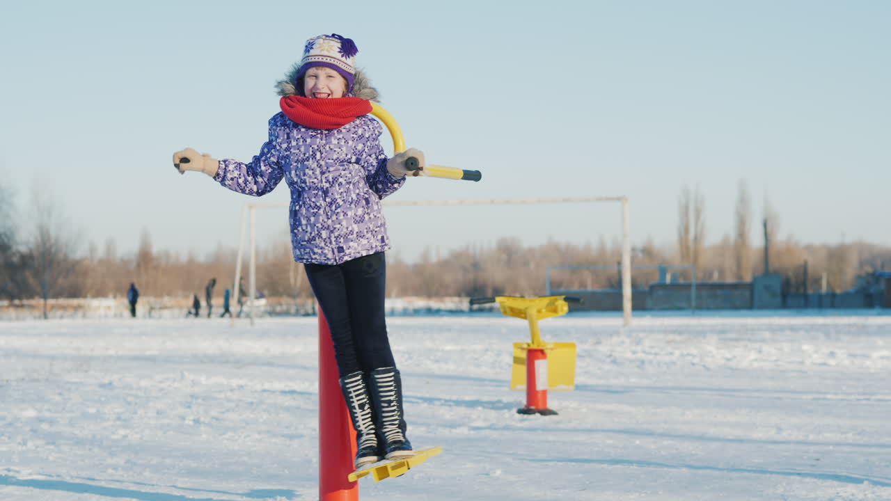 una niña con ropa abrigada está jugando en el patio de la escuela montando un entrenador de fitness