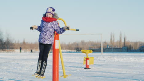 a girl in warm clothes is playing in the schoolyard riding a fitness trainer