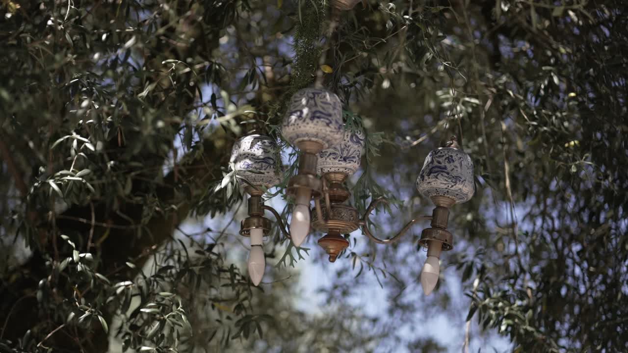 blue white ceramic chandelier suspended among leafy tree branches