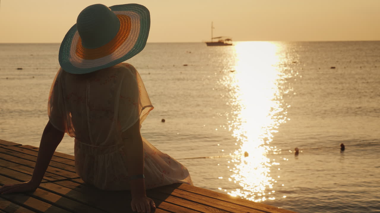 una joven se encuentra con el amanecer en el muelle, se sienta y mira el sol y el barco en el mar dre