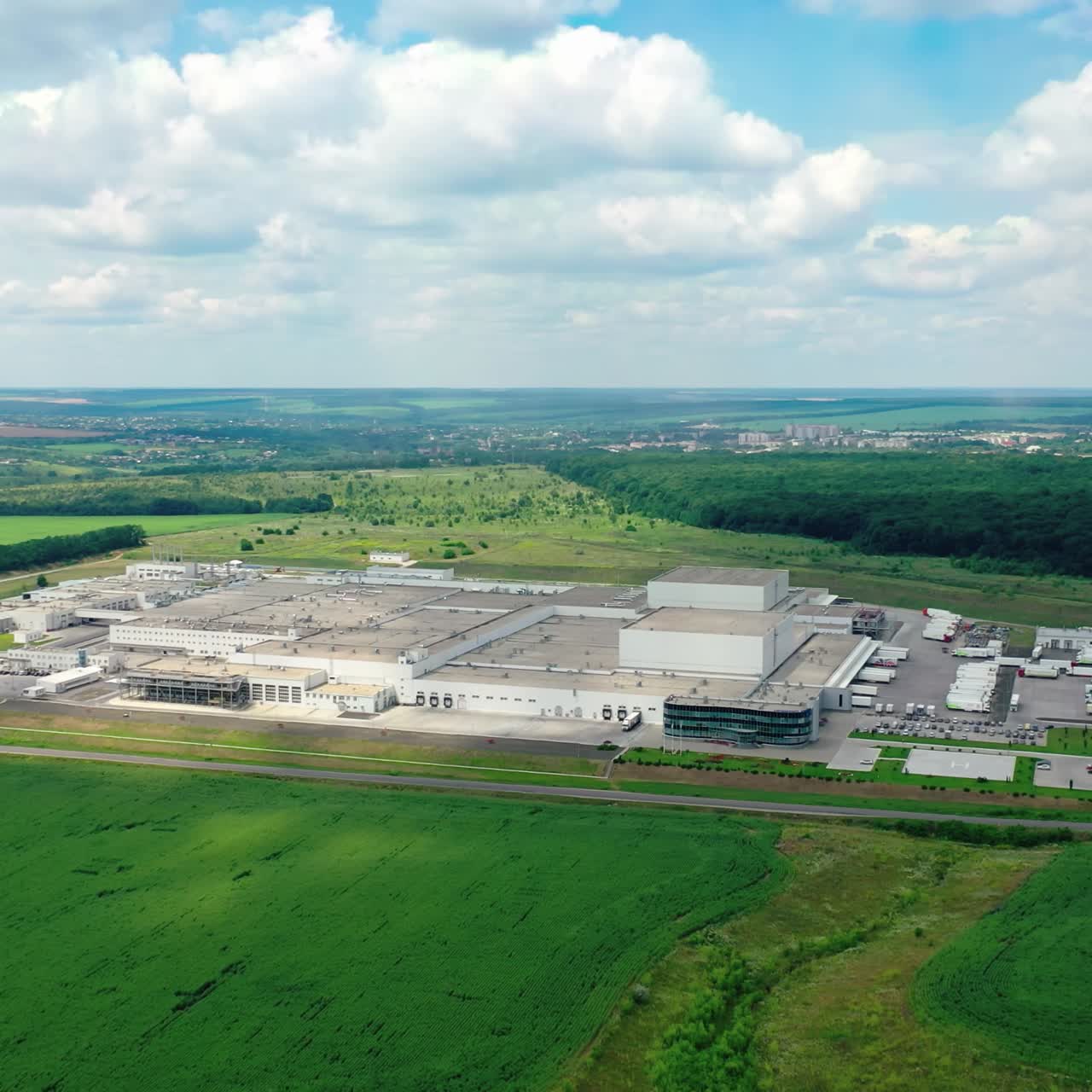 Large factory outside the city. Industrial plant on green fields and forests background. View from above on a modern industrial area among nature. Aerial view