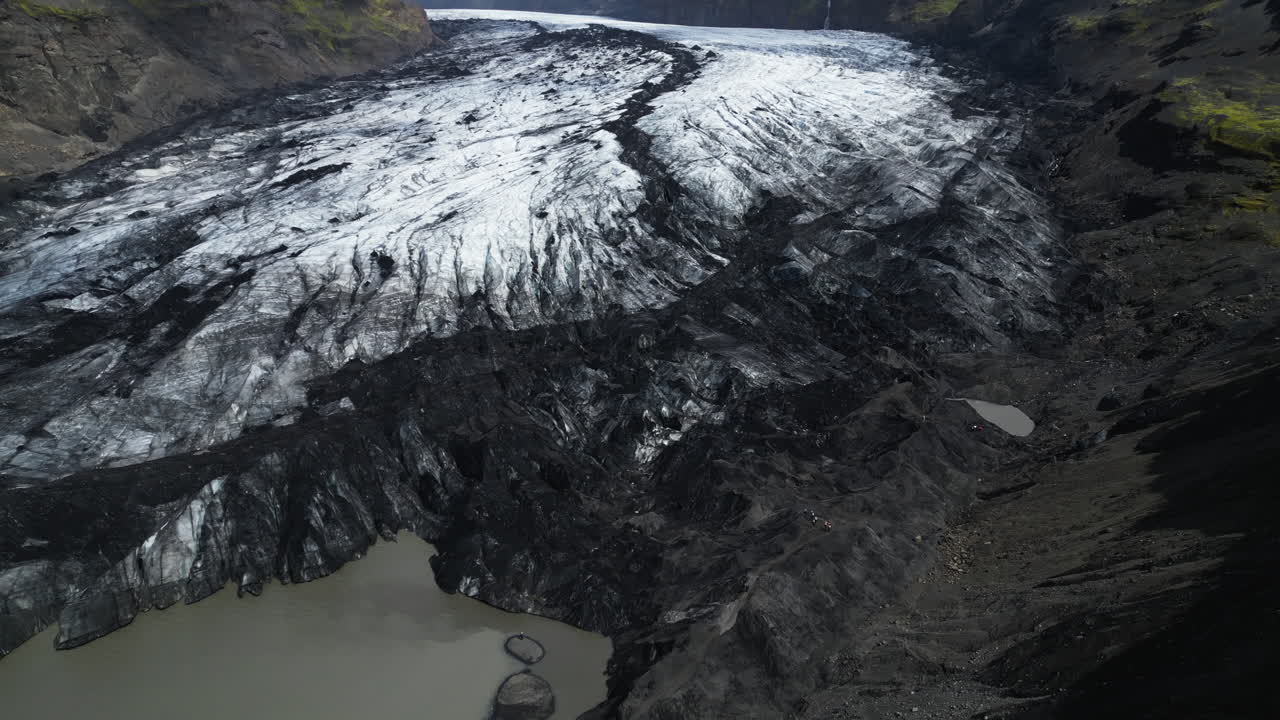 Dramatic Landscape Of Ice Streaked With Dark Volcanic Ash At Sólheimajökull Glacier In Iceland. Aerial Shot