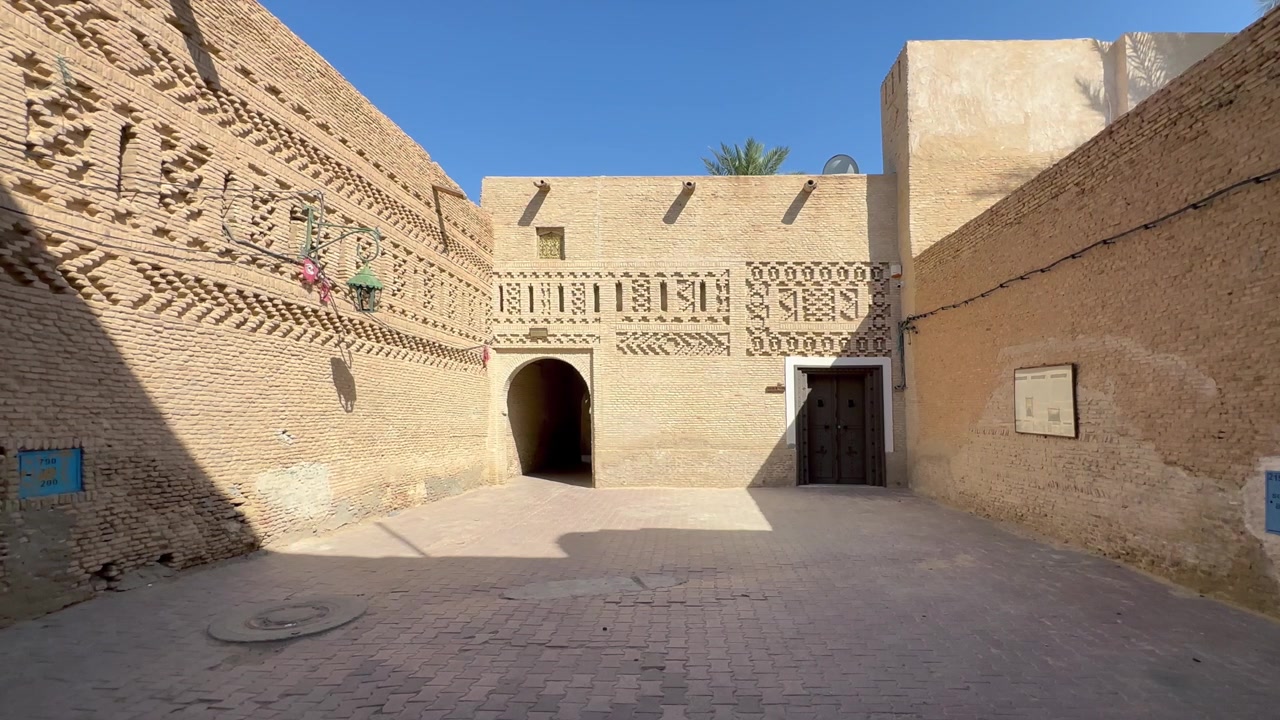 Cortile tradizionale in mattoni con muri in adobe intagliati, passaggio ad arco e porte in legno nella medina di Tozeur, Tunisia