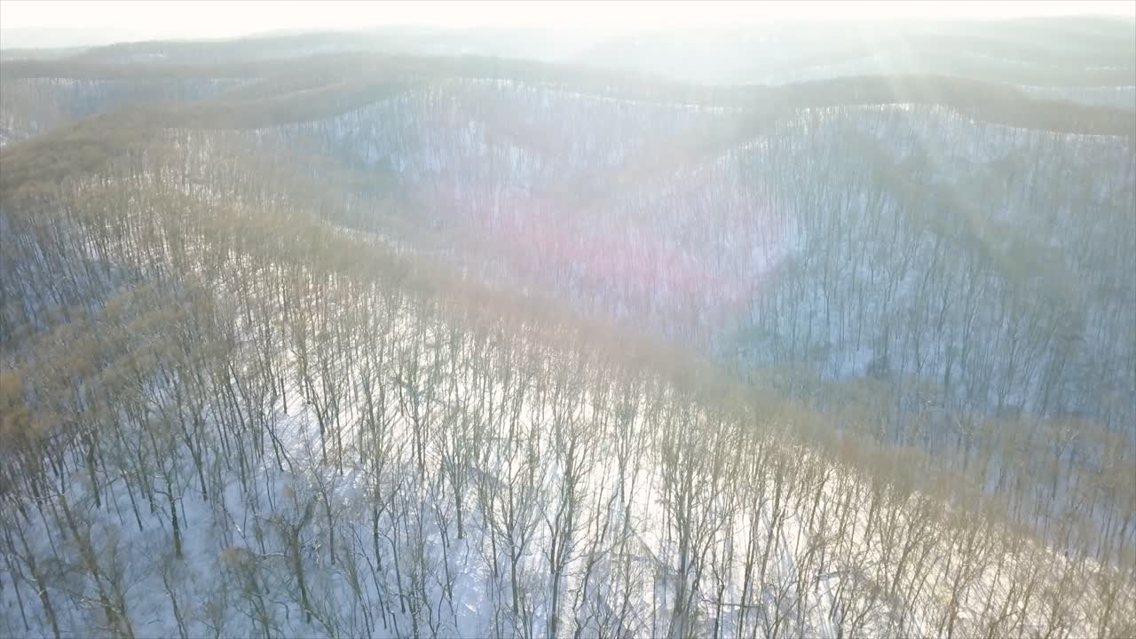 Aerial drone shot with sun and lens flares over snowy landscape of a frozen forest in Midwestern Missouri