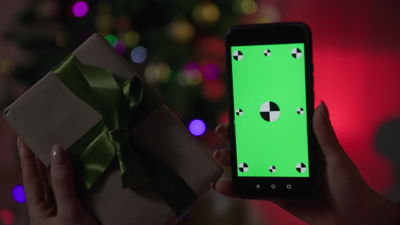 새해 선물, 여성 손은 녹색 화면과 선물을 가진 휴대 전화를 들고 크리스마스 트리의 배경에 밤에 카메라 앞에