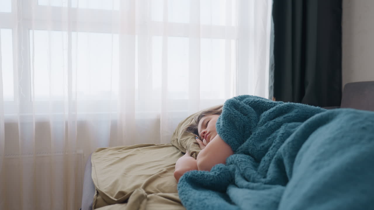 Donna rilassata sul divano, donna serena sdraiata sul divano avvolta in una morbida coperta con luce soffusa, donna tranquilla distesa sul divano ornato di tessuti materici durante una calma giornata di sole