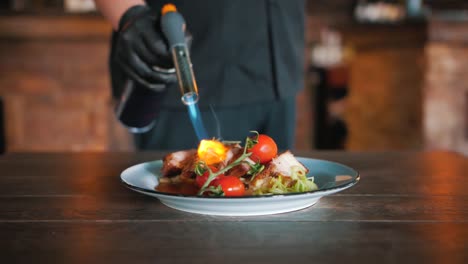 chef finishing a dish with meat and tomatos with a culinary torch