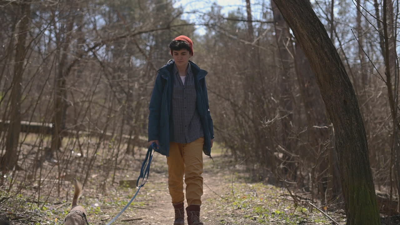 молодая женщина с короткими волосами гуляет с собакой в лесу