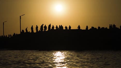 Silueta-De-Un-Grupo-De-Personas-Caminando-En-El-Muelle-Del-Mar-Al-Atardecer