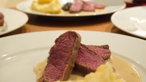 a white male hand model is serving a red lamb meat on a morel sauce next to mashed potatoes on a white platze in slow motion