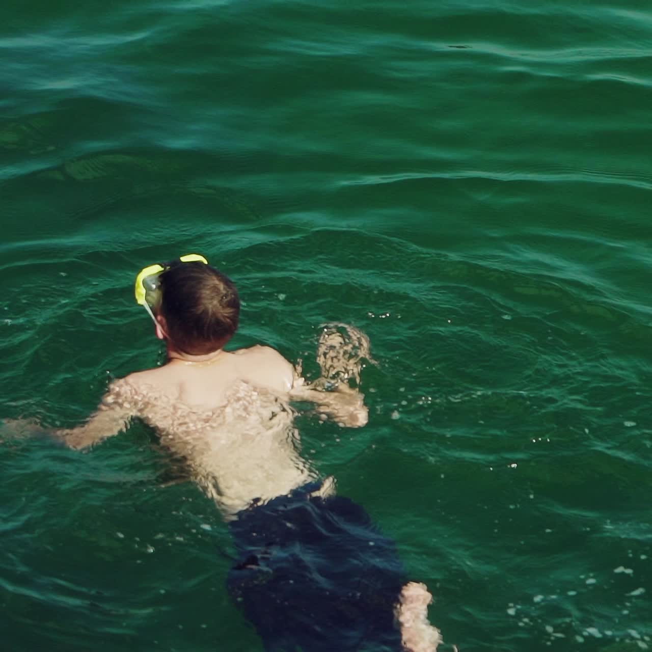 guy in blue shorts is swimming under water in a mask in the sea in the summer. Slow motion