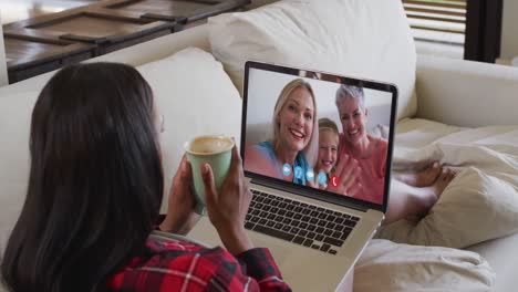 Afroamerikanische-Frau-Hält-Eine-Kaffeetasse-In-Der-Hand-Und-Führt-Einen-Videoanruf-Auf-Dem-Laptop,-Der-Zu-Hause-Auf-Der-Couch-Sitzt