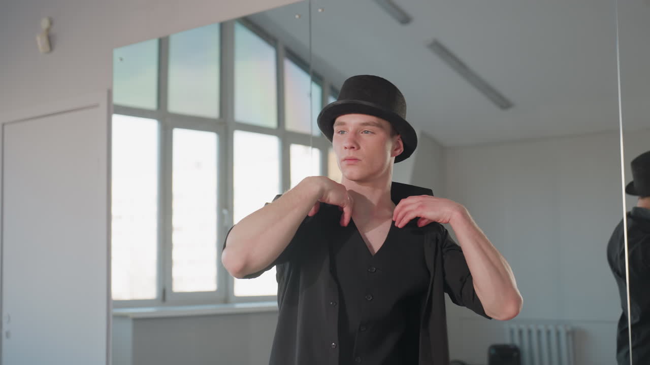 stunning student wearing top hat and vest slips into black jacket in bright studio mirror reflecting neck tattoo intense gaze smooth elegant motion highlighting masculine style urban loft setting