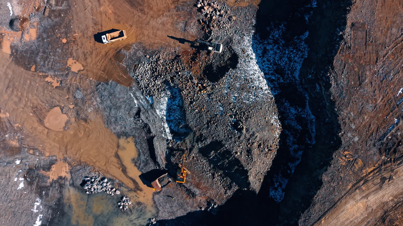 Overhead view of excavators loading trucks in quarry. Top down shot of hydraulic excavators and dump trucks working on rock piles in a stone mine