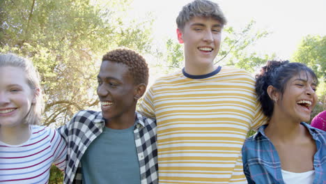 portrait of happy diverse group of teenage friends embracing in sunny park, slow motion