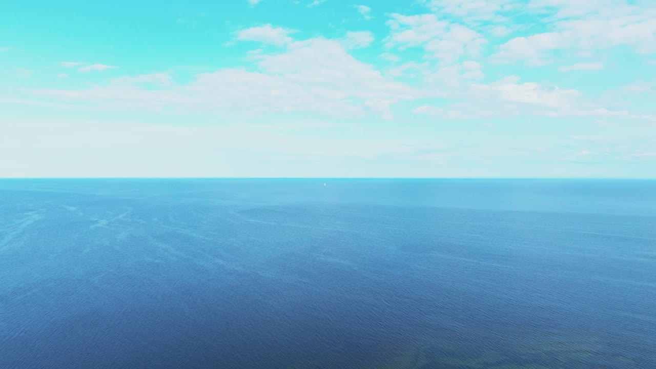Backwards flying shot over sea, small sailboat visible in the distance
