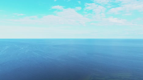 backwards flying shot over sea, small sailboat visible in the distance