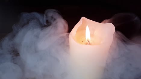 haunted theme and scary white smoke fog rolling over an old oak table with a dark background over and past a burning candle flame