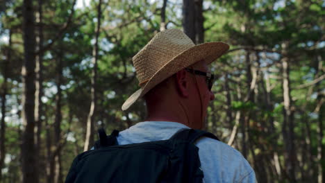 older european man with grey beard looks around in forest wearing sunglasses and woven fiber hat