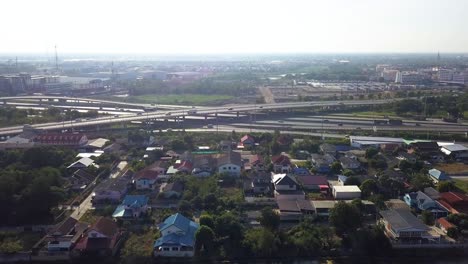 Himmelsblick-Auf-Kreuz-Und-Quer-Verlaufende-Autobahnen-Mit-Laufenden-Fahrzeugen-In-Thailand,-Umgeben-Von-Häusern-Und-Grünen-Pflanzen---Luftaufnahme