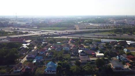 sky view of a crisscross highways with running vehicles in thailand surrounded with houses and green plants - aerial shot