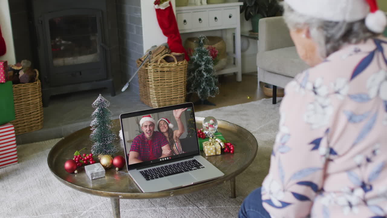 mujer caucásica mayor usando una computadora portátil para una videollamada de navidad con una pareja sonriente en la pantalla