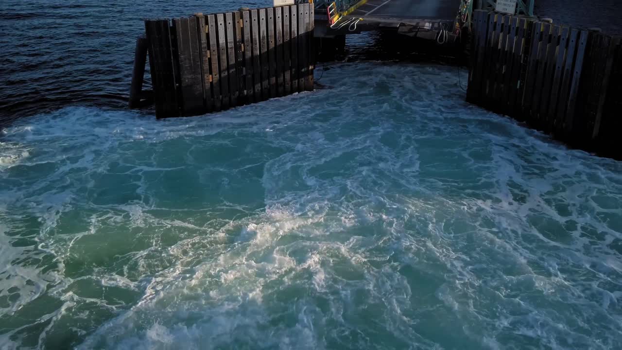 Slow pan up of ferry docking at Point Defiance terminal, Tacoma Washington, prop wash, emerald blue green water, sunset shadows