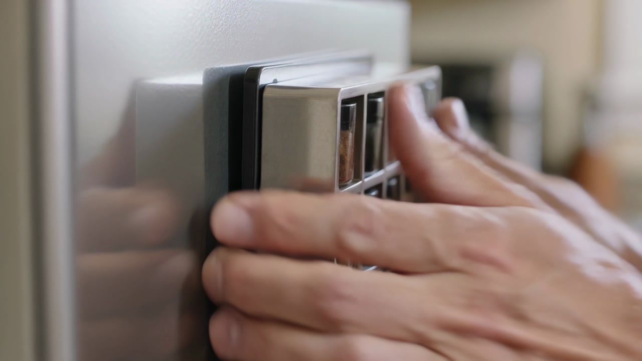 Placing male-presenting hands on keypad against metallic front in study, pressing buttons to unlock