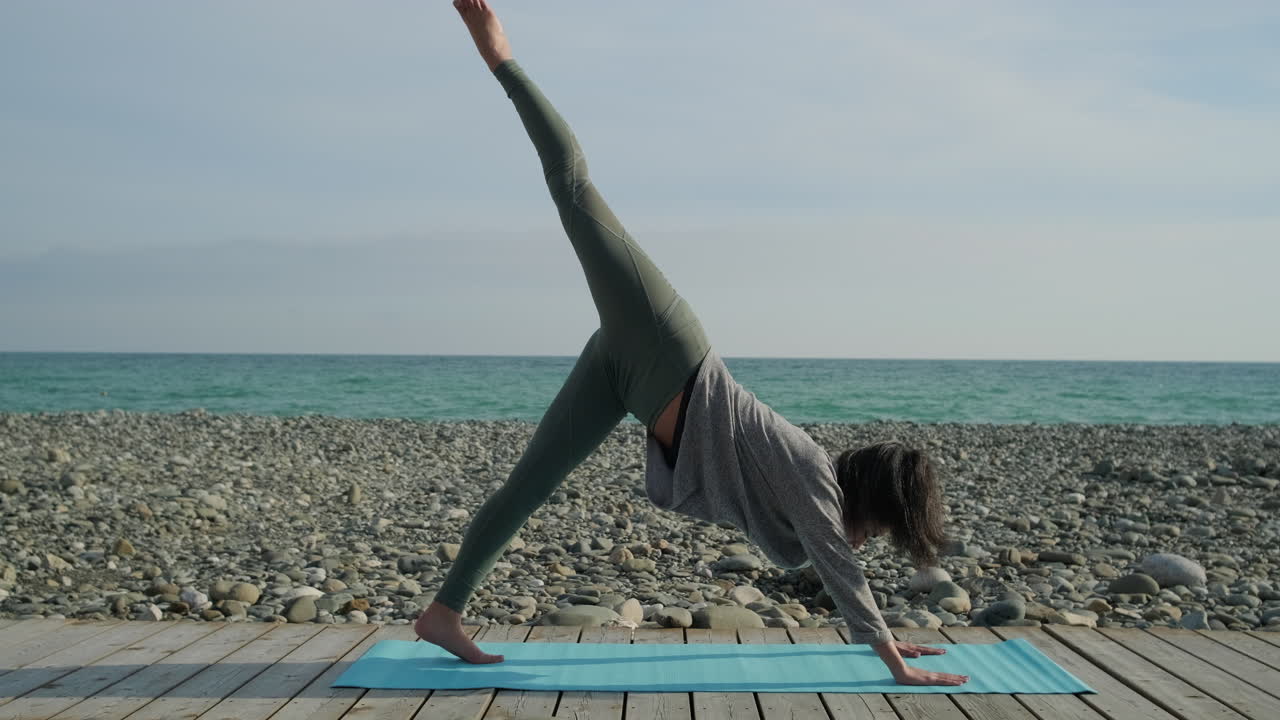 mujer practicando la postura de yoga del perro hacia abajo en la playa