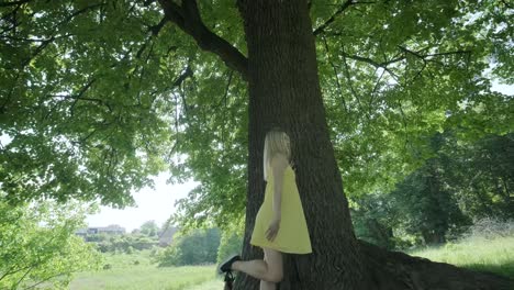 woman in yellow dress dancing by tree in summer park