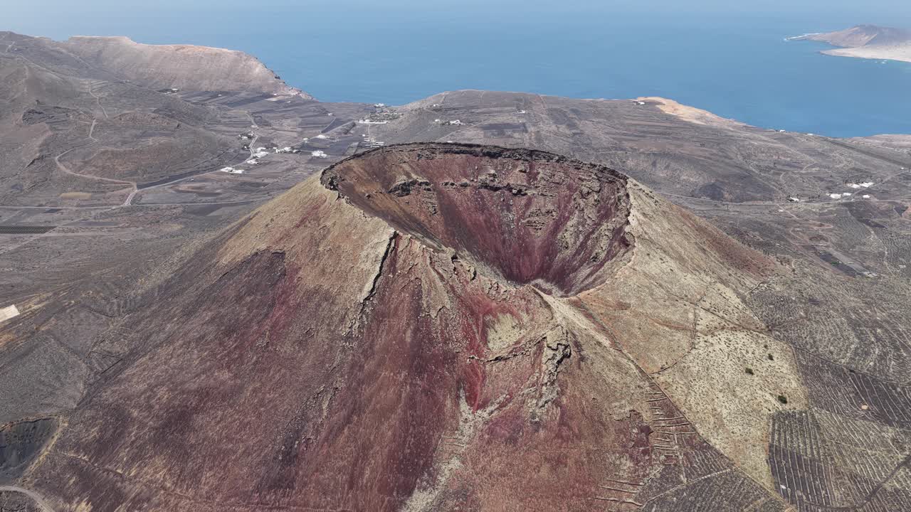 Volcan de la Corona Crater On Volcanic Plains In Lanzarote, Spain With Atlantic Ocean In Background. aerial pullback shot