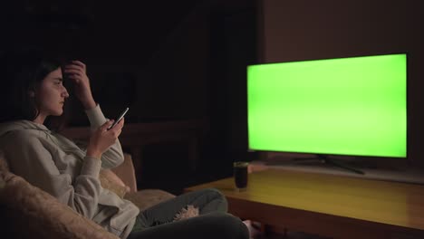 girl sitting on the sofa watching tv and texting messages sitting on sofa