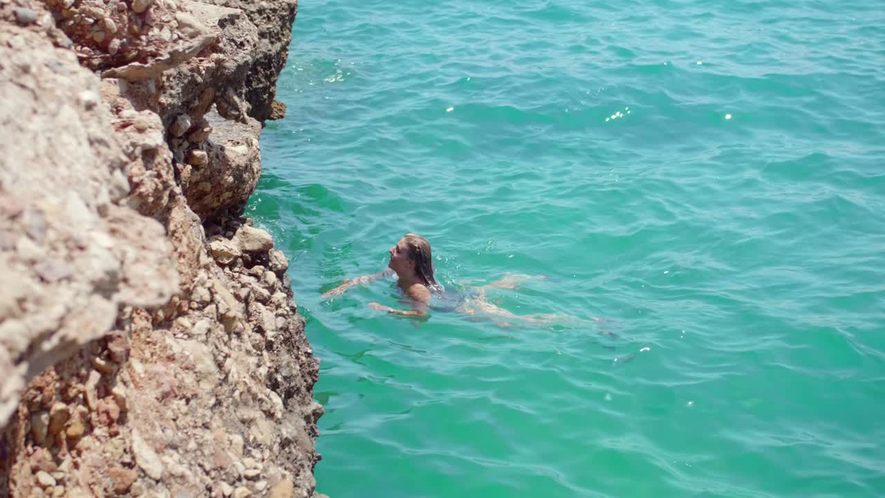 mujer sexy nadando en un mar azul brillante hacia la costa escarpada en verano