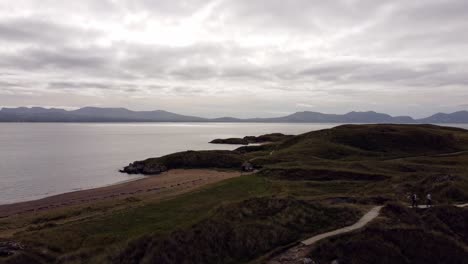 Vista-Aérea-Aérea-Ynys-Llanddwyn-Island-Anglesey-Sendero-Costero-Con-Montañas-Snowdonia-A-Través-Del-Mar-Irlandés