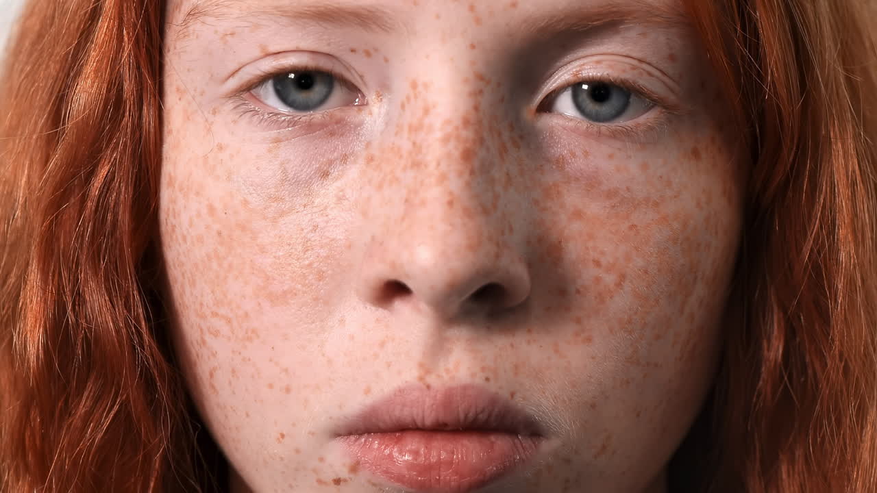 Red haired girl with lots of freckles on the face and blue eyes looking into the camera. Close up