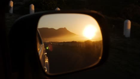 sunset next to mountain caught in side-mirror of driving car