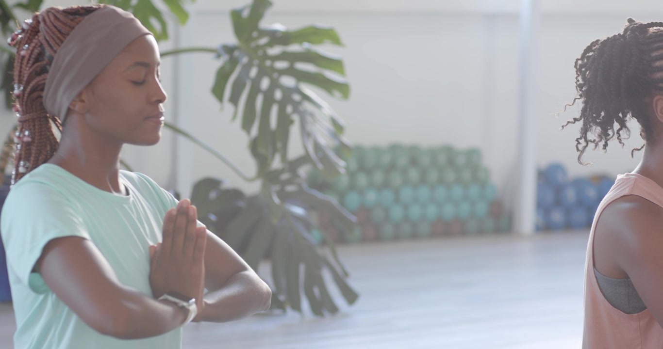 Två kvinnliga vänner sitter på yogamattor och mediterar, centrerar sig medan kameran panorerar, en klocka syns.