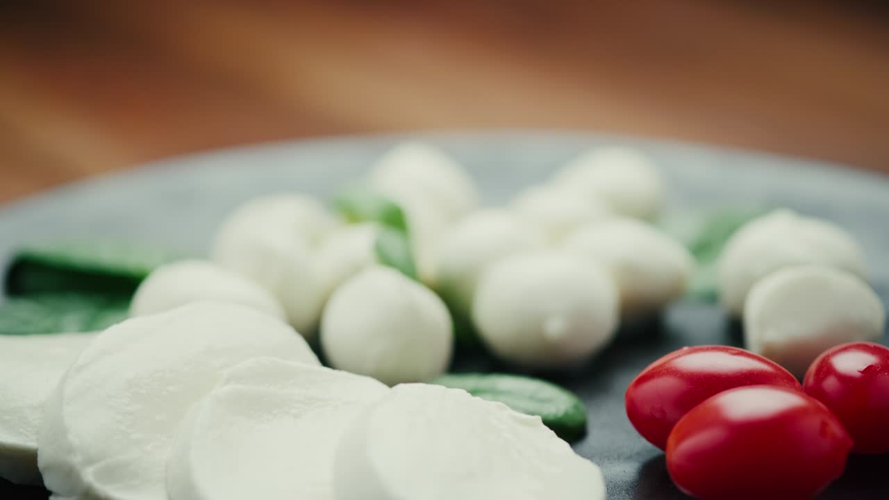 소형 모자라 치즈 볼, 스파나치 잎, 토마토를 검은 접시 위에 넣는다.