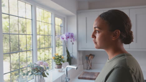 Mujer-Soldado-Pensativa-En-Uniforme-En-La-Cocina-Durante-El-Permiso-En-Casa-Mirando-Por-La-Ventana