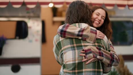 A-happy-brunette-girl-in-a-plaid-shirt-jumps-into-the-arms-of-her-brunette-boyfriend-in-a-green-plaid-shirt-and-hugs-him-during-their-vacation-in-a-camp-near-a-trailer-outside-the-city-in-the-summer