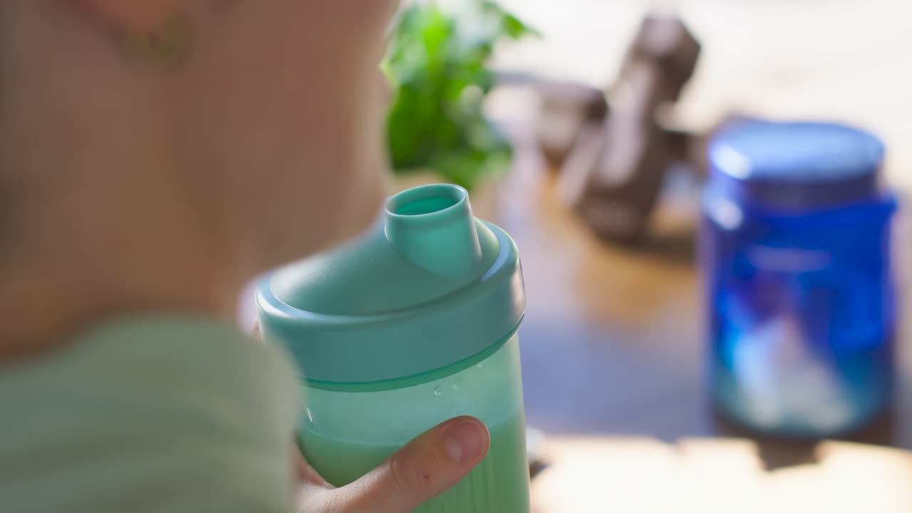 Un bambino sta capovolgendo il coperchio di uno spargi-menta e sta alzando la bottiglia per bere, mentre una mano si stabilizza sul tavolo della cucina.