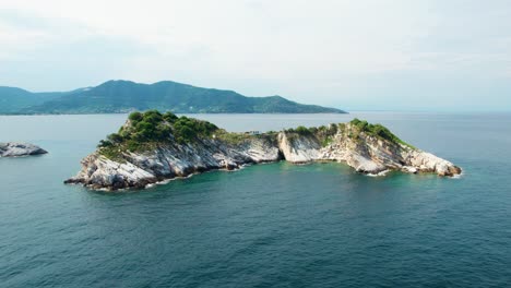 cinematic aerial view of gramvousa island with a white church, surrounded by the mediterranean sea, birds flying, high mountain peaks, green vegetation, thassos, greece